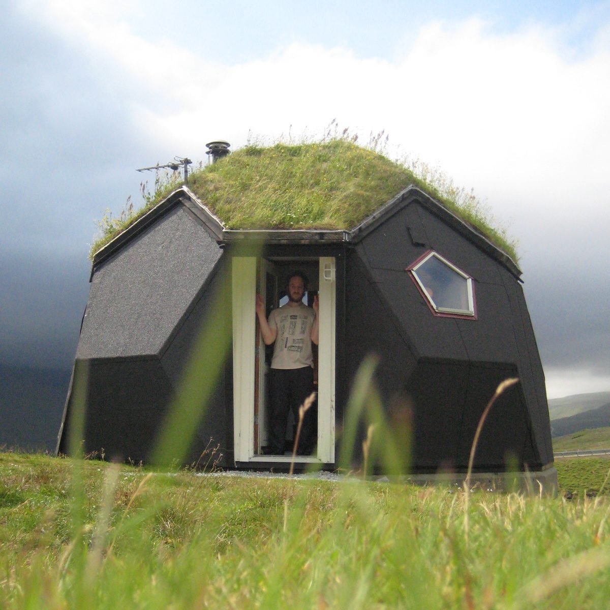 Black geodesic dome with grass roof on hillside