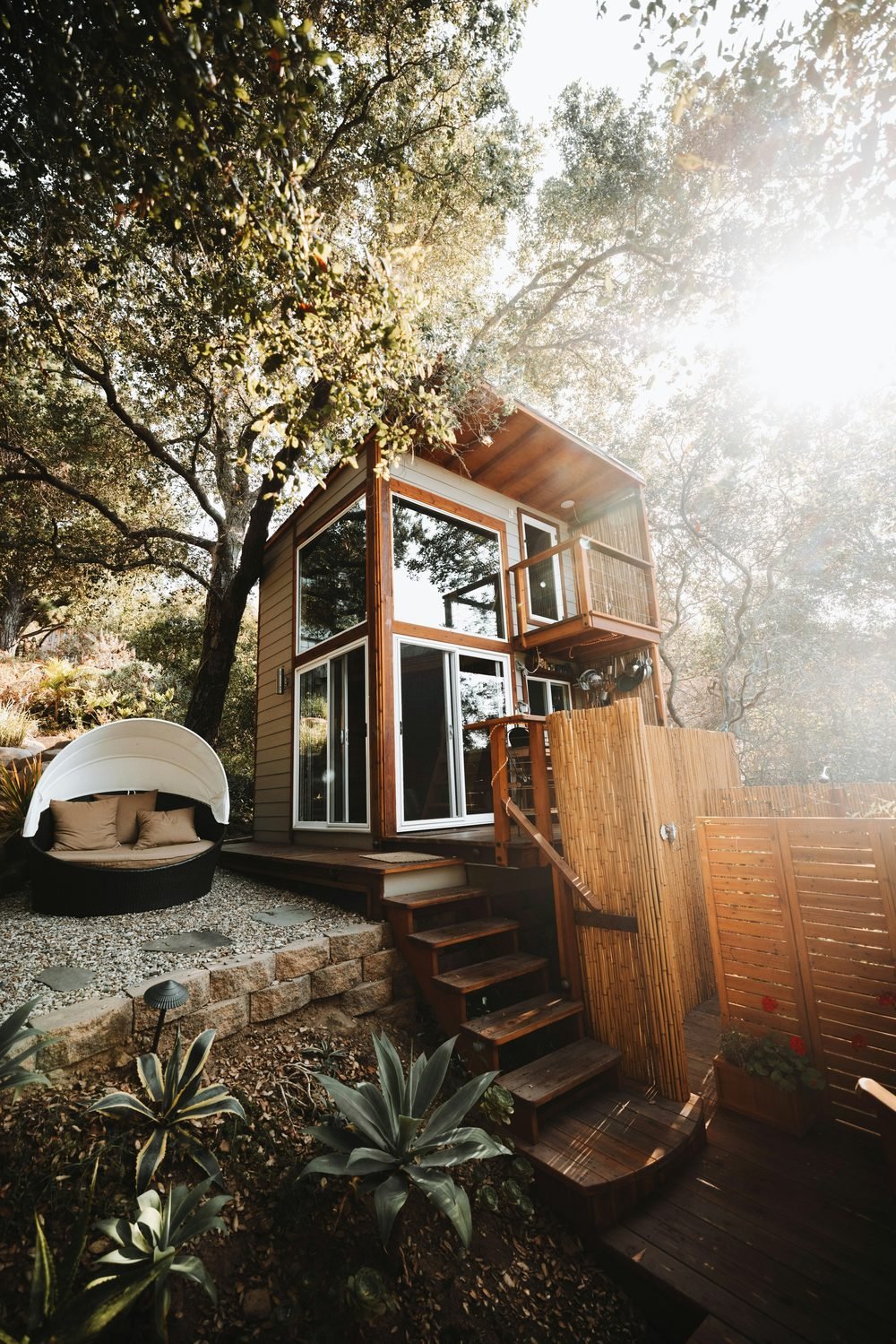 Two-storey timber cabin in garden, sunlight through trees