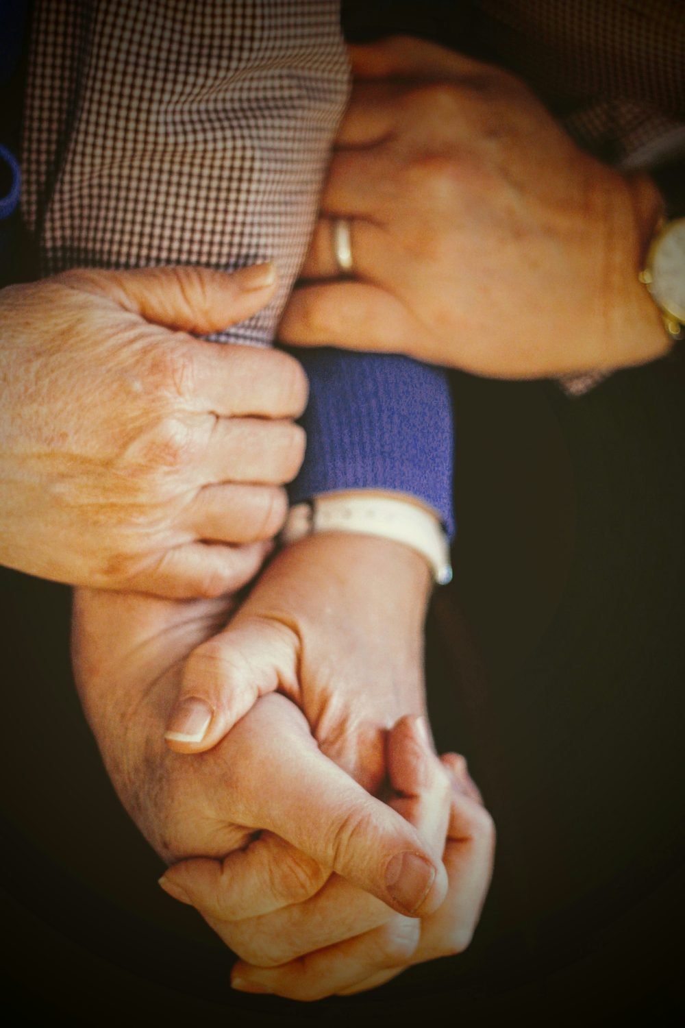 An elder's weathered hands holding a baby's hand — bridging the generations